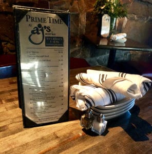 Prime time table tent menu and a stack of plated with silverware roll ups. 